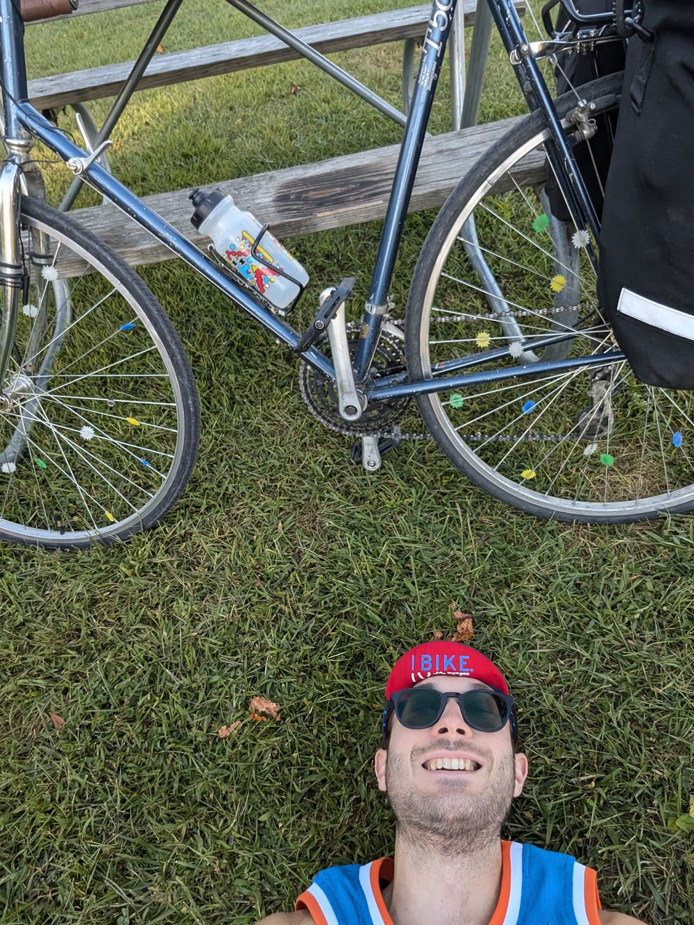 Peter lying in the grass beside his loaded touring bicycle, grinning up at the camera